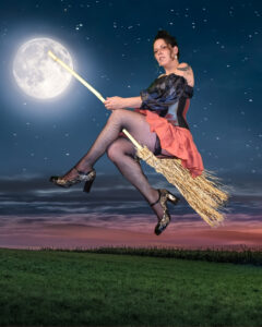 Woman riding a broomstick in front of the moon in an orang fluffy skirt with an iridescent corset